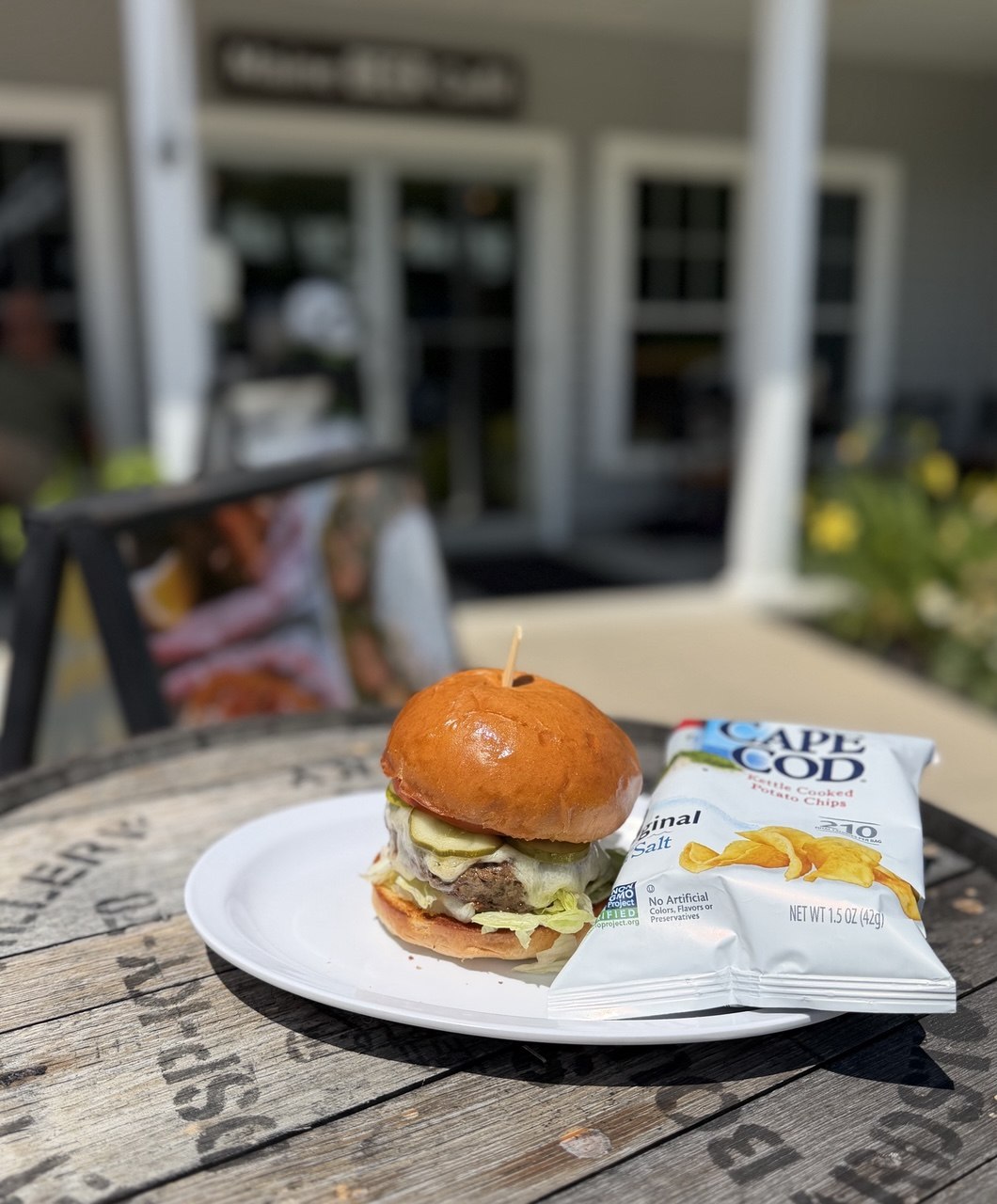 Cheeseburger with pickles and Cape Cod chips on a barrel table outside the cafe